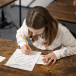 Kind in weissem Langarm schreibt eine Prüfung auf einem hölzernen Tisch